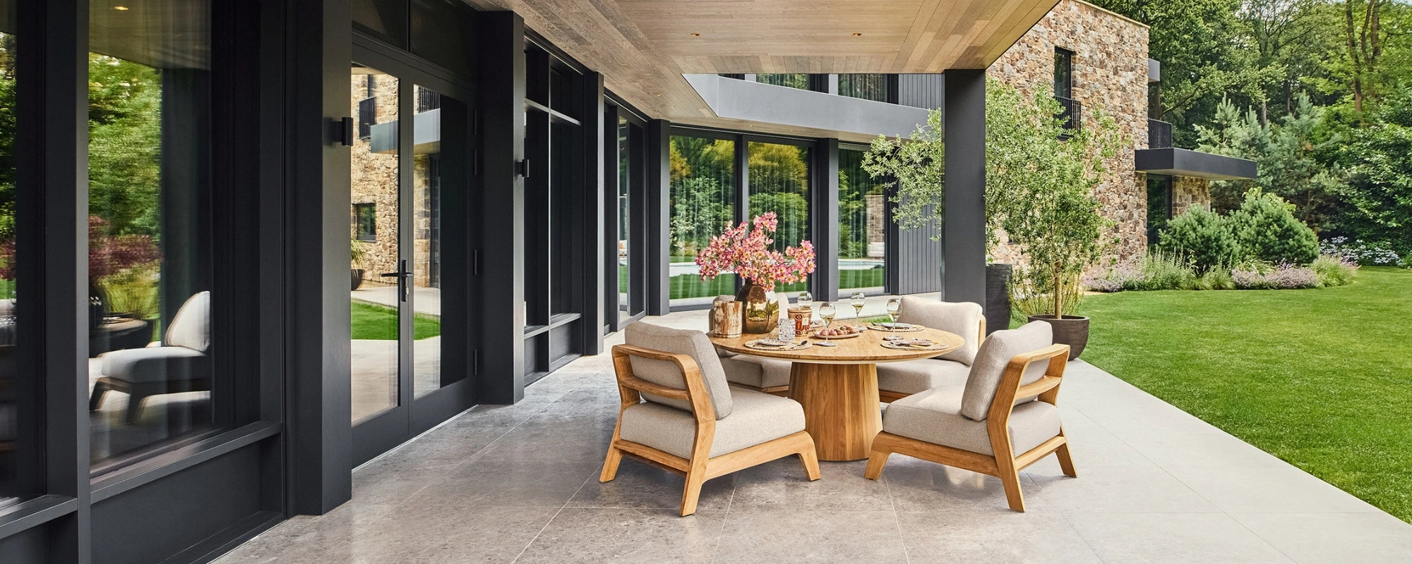 Modern outdoor patio with wooden low dining table and chairs, surrounded by a garden.